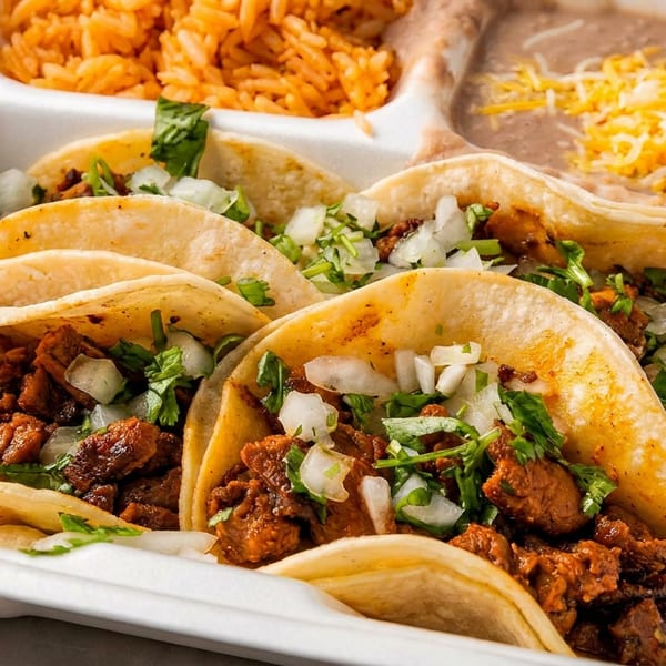 Four street tacos with meat, onions, and cilantro, alongside rice and refried beans with cheese.