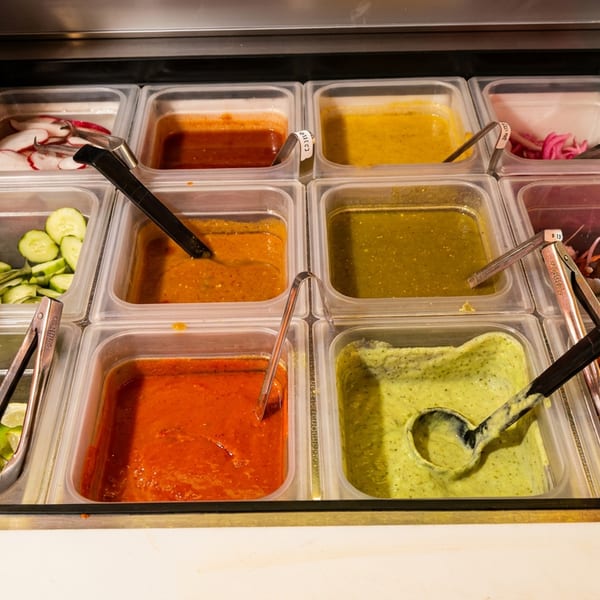 A self-serve salsa bar with various red and green salsas, pico de gallo, limes, cucumbers, and radishes.