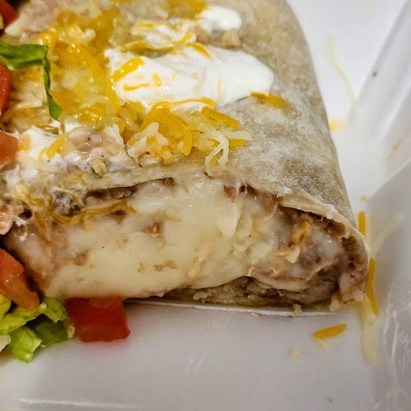 Close-up of a burrito cut open, revealing melted cheese, meat, and toppings in a white container.
